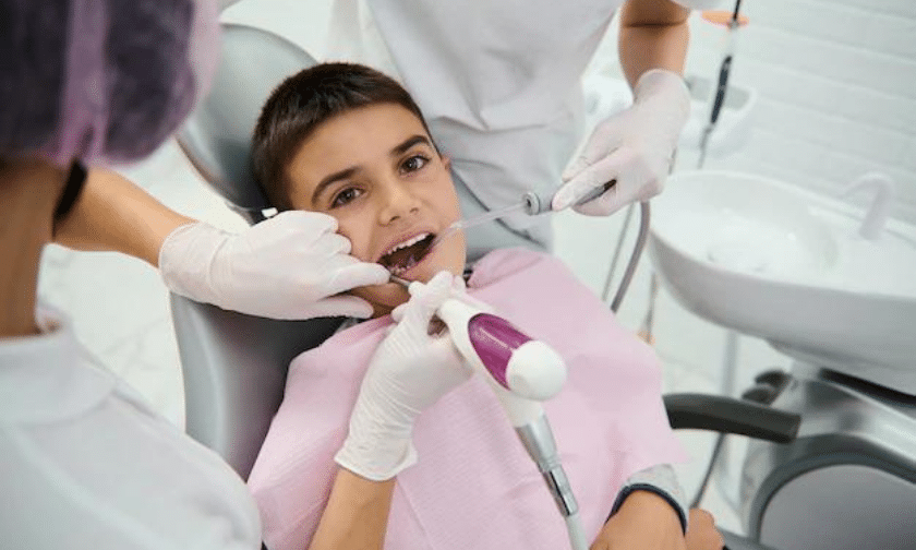 Young patient receiving orthodontic examination in dental chair with gloved dentist hands visible.