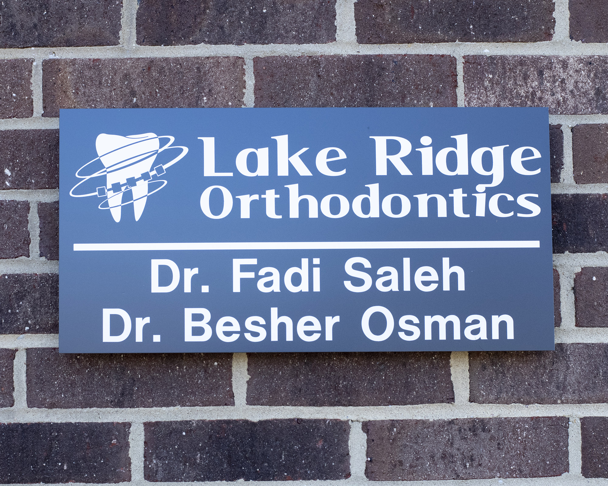 Lake Ridge Orthodontics business sign with doctors' names mounted on brick wall.
