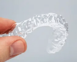 Clear plastic orthodontic retainer held between fingers against white background