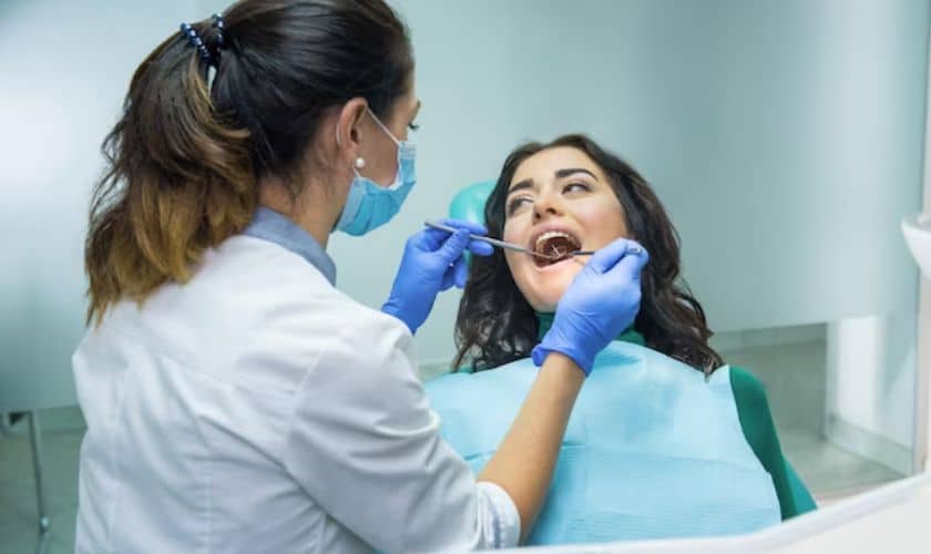 Dentist in blue gloves examines patient's teeth in clinical dental office setting.