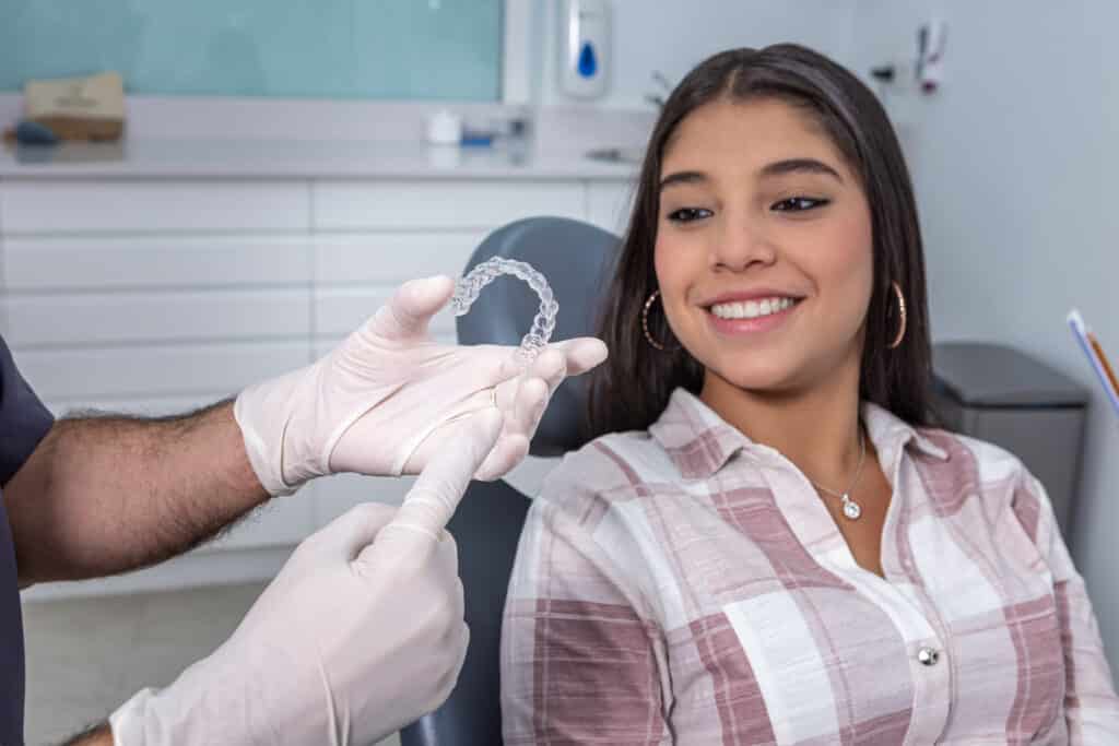 A woman smiles at a dentist showing her a clear dental aligner. The dental office is bright and clean, conveying a sense of professionalism and care.
