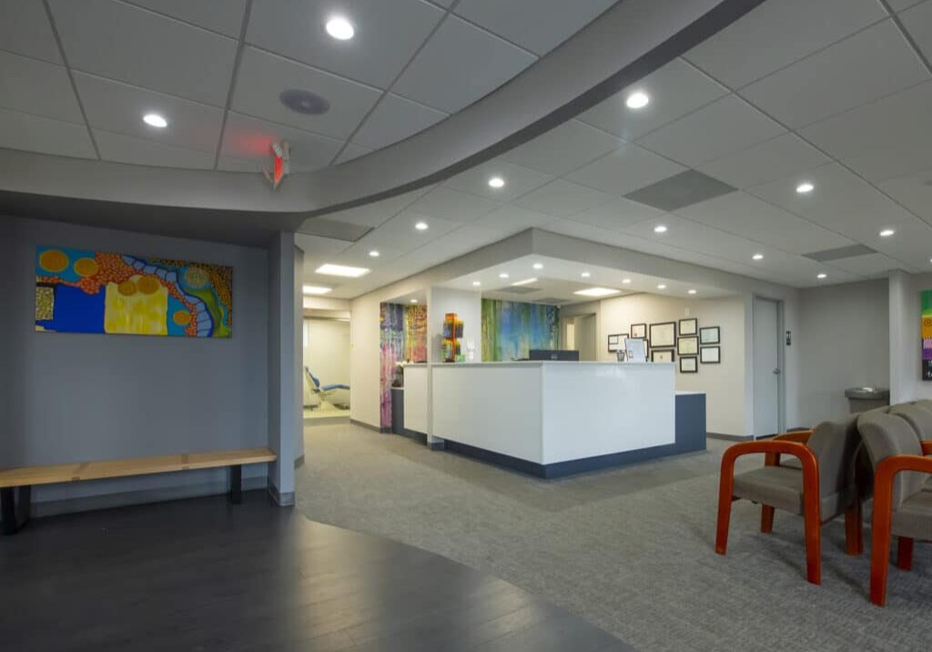 Modern orthodontics clinic reception area with clean flooring, front desk, and colorful wall art.