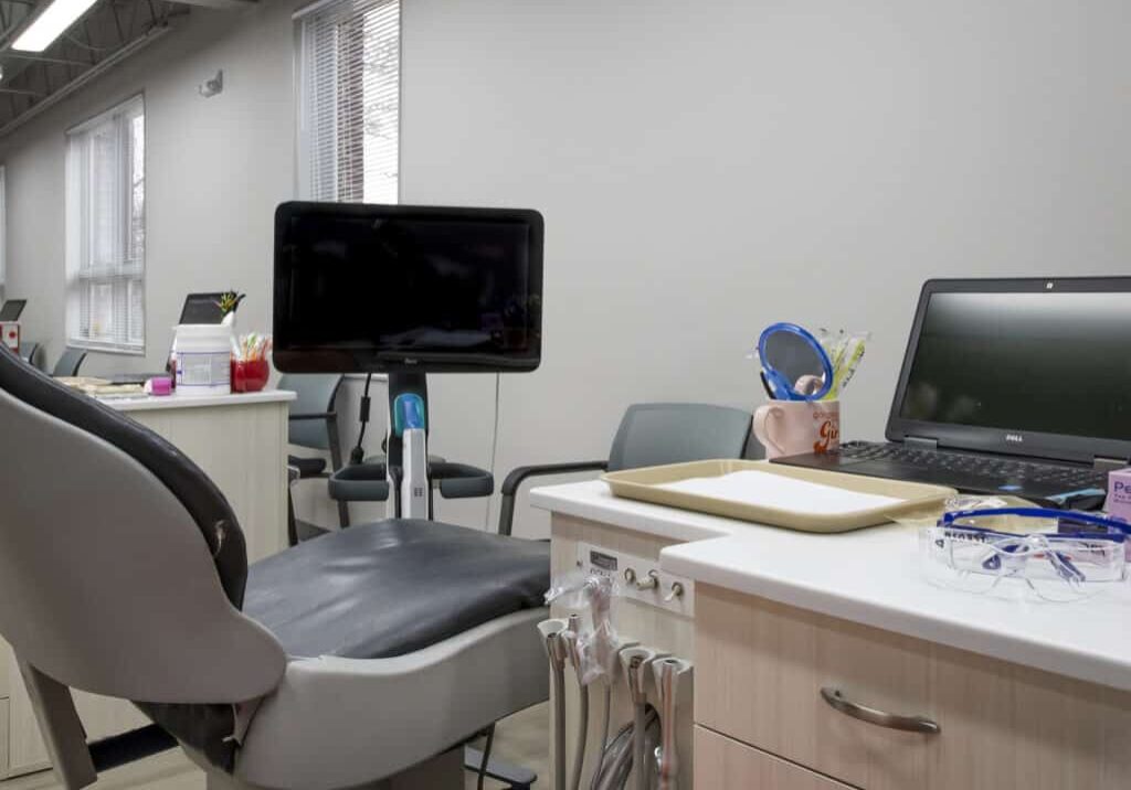 Modern orthodontics office treatment room with dental chair, monitor, and equipment.