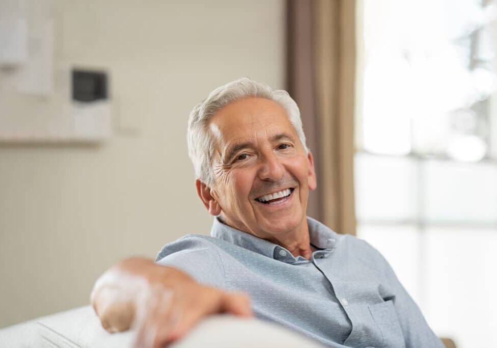 Smiling older man in blue shirt relaxing indoors near window, professional portrait setting