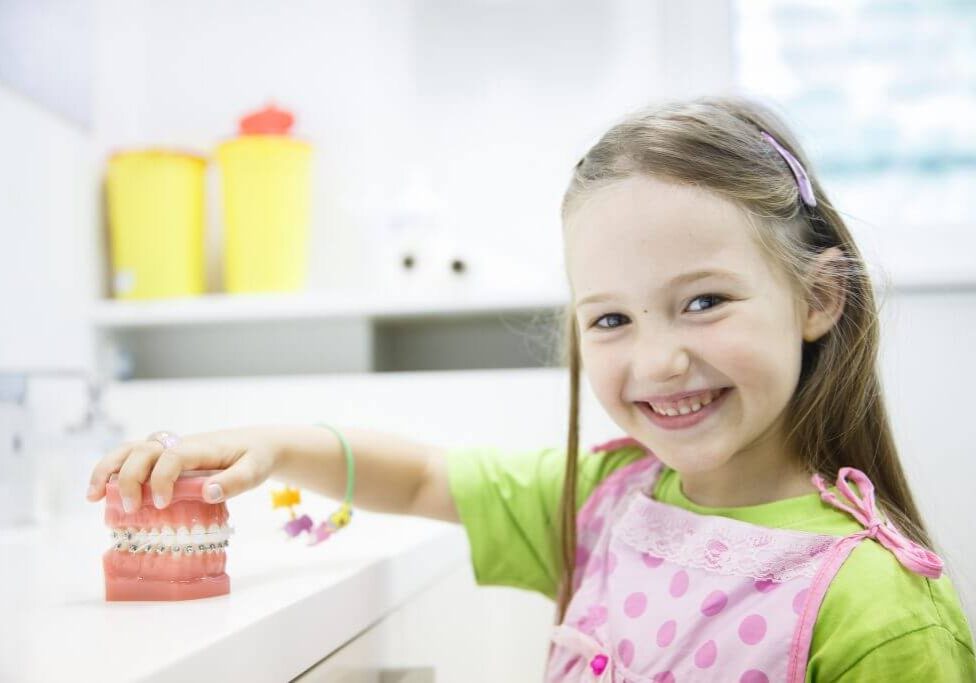 Young girl smiling while reaching for items in bright, modern kitchen with white cabinets.