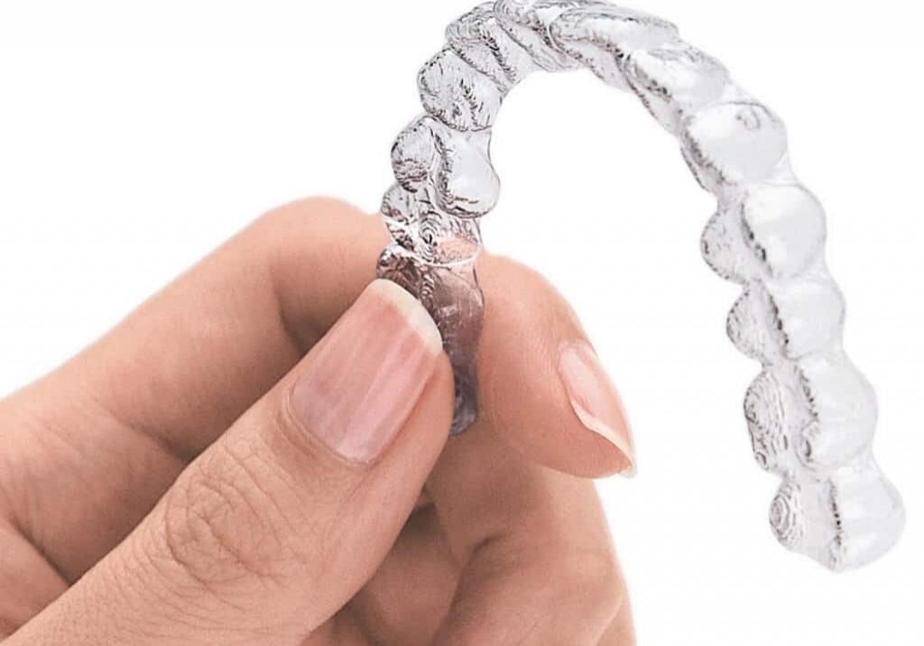 Hand holding clear orthodontic aligner tray showing transparent dental correction device.